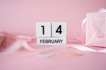Top view of February 14 wooden calendar blocks on pink background with gift boxes and ribbons. Valentine's Day flat lay concept.