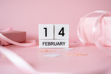 Top view of February 14 wooden calendar blocks on pink background with gift boxes and ribbons. Valentine's Day flat lay concept.