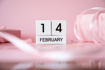 Top view of February 14 wooden calendar blocks on pink background with gift boxes and ribbons. Valentine's Day flat lay concept.