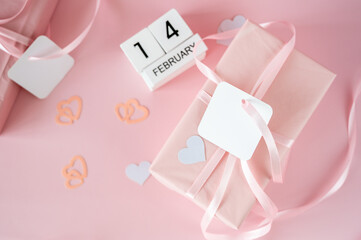 Top view of February 14 wooden calendar blocks on pink background with gift boxes and ribbons. Valentine's Day flat lay concept.