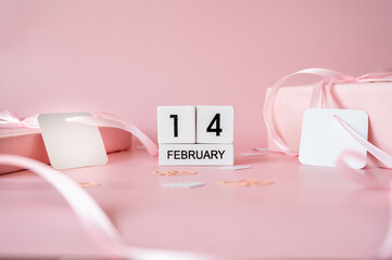 Top view of February 14 wooden calendar blocks on pink background with gift boxes and ribbons. Valentine's Day flat lay concept.