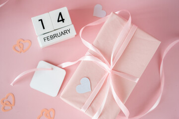 Top view of February 14 wooden calendar blocks on pink background with gift boxes and ribbons. Valentine's Day flat lay concept.