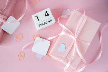 Top view of February 14 wooden calendar blocks on pink background with gift boxes and ribbons. Valentine's Day flat lay concept.