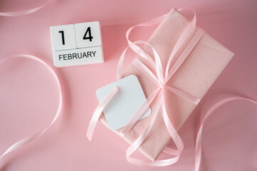 Top view of February 14 wooden calendar blocks on pink background with gift boxes and ribbons. Valentine's Day flat lay concept.
