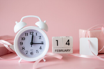 White alarm clock with pink gift boxes and blank gift tags on pink background. Time for celebration, Valentine's Day concept