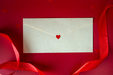 Craft paper envelope with red heart seal on red background with silk ribbon. Valentine's Day love letter concept