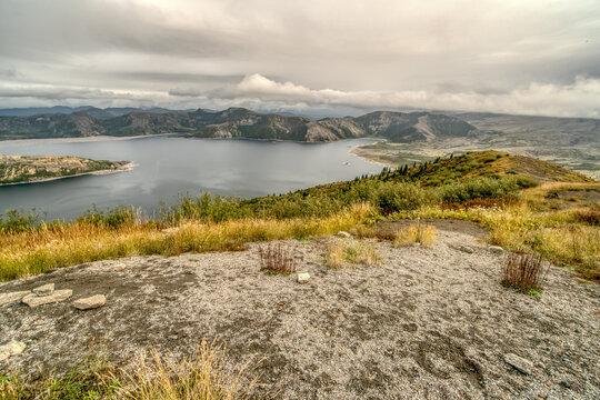 A mountain top with a lake in the distance. The sky is cloudy and the view is serene