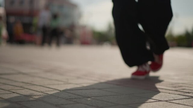 red sneakers crossing open urban plaza with lowangle cinematic framing, blurred crowd in background and long shadow trailing behind, casual stride with light bounce, outdoor city scene in warm