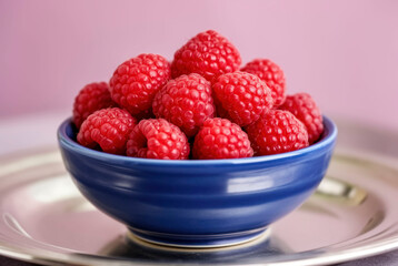 A vibrant close up showcases a generous portion of ripe raspberries presented beautifully within a striking blue bowl on a silver platter. This image is perfect for food related projects.