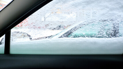 Frozen car window covered with snow and ice seen from inside the vehicle in winter. Cold weather concept, icy texture on glass, urban winter conditions, transportation and seasonal background