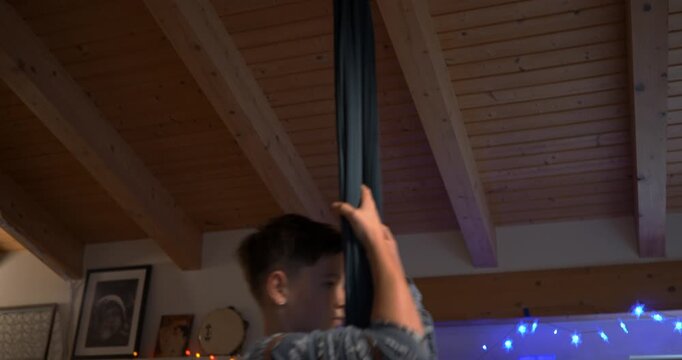 Suspended in Air: A youthful individual finds balance and strength suspended gracefully on aerial equipment, with the soft glow of interior lighting enhancing the atmosphere.