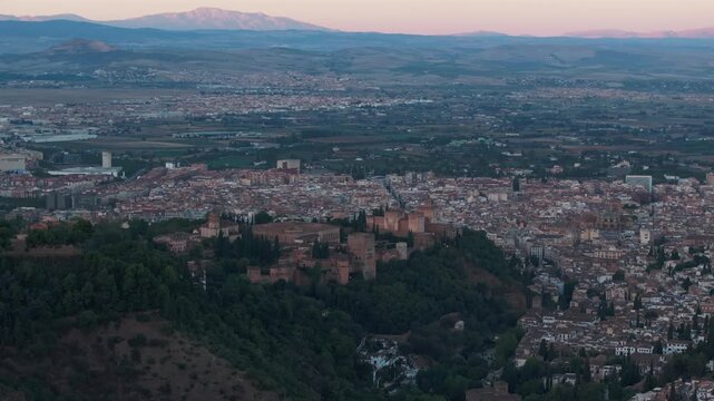 Wide drone aerial of Granada at sunrise with the Alhambra on the hill, soft haze and long shadows across the city, Andalusia Spain