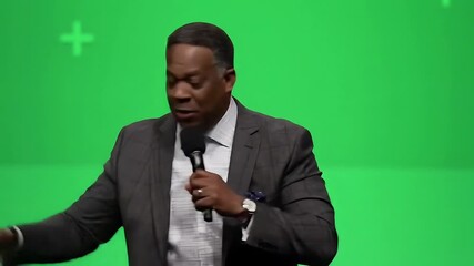 Lockdown of a man in a formal suit standing against a green screen backdrop, making gestures, and speaking fervently into a 4K microphone