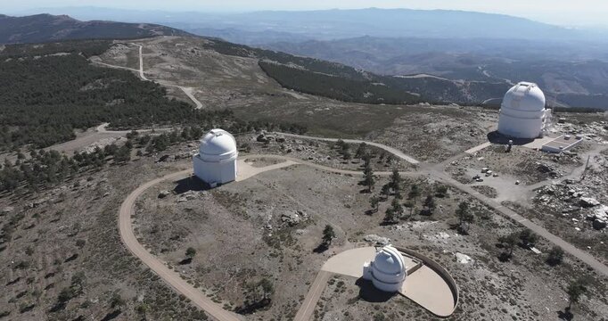 Drone aerial orbit of Calar Alto Observatory, Tabernas Spain, multiple telescope domes on rugged mountain plateau with winding access roads