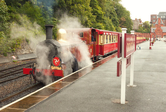 The red steam locomotive with train of IMR line in puffs of vapour prepares to depart from the platform of Douglas railway terminal station. Isle of Man, UK