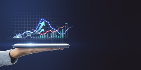 Hand holding digital tablet with colorful financial graphs, candlestick charts and rising arrow emerging from screen, representing mobile trading, real time analytics and modern investment technology

