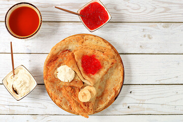 Delicious Russian pancakes with soft cheese, bananas, and honey on the kitchen table. A healthy breakfast made from fresh ingredients, the Maslenitsa concept and traditional Russian cuisine