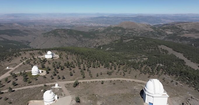 Wide drone aerial showing Calar Alto Observatory domes in Tabernas, Spain, arid ridgelines and distant mountain ranges under clear sky