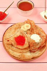 Delicious Russian pancakes with soft cheese, bananas, and red caviar on the kitchen table. Healthy breakfast with fresh ingredients, Maslenitsa concept and traditional Russian cuisine, selective focus