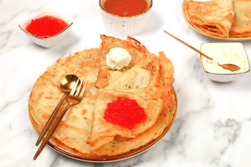 Delicious Russian pancakes with soft cheese, bananas, and red caviar on a marble table. Healthy breakfast with fresh ingredients, Maslenitsa concept and traditional Russian cuisine