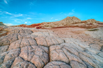 A rocky, barren landscape with a blue sky in the background. The sky is dotted with clouds, and the sun is shining brightly. The scene is peaceful and serene