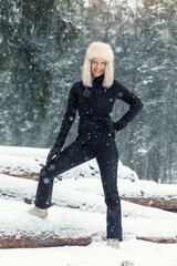 Portrait young adult mid age smile woman enjoy have fun walking in park forest snowfall cold winter day. Female portrait person happiness wear black ski overall stylish fur hat snowflakes background