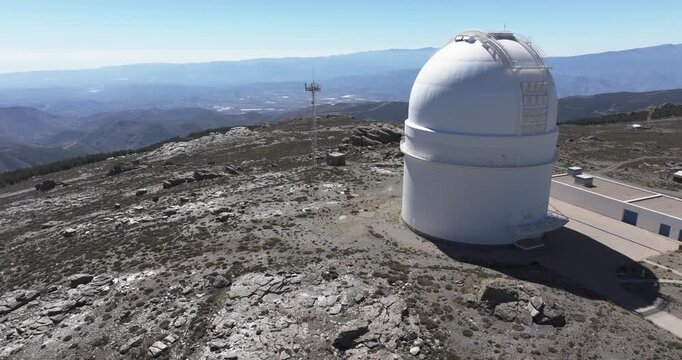 Drone aerial pass by Calar Alto Observatory dome, Tabernas Spain, white radome against rugged rocky landscape and distant mountain ridges