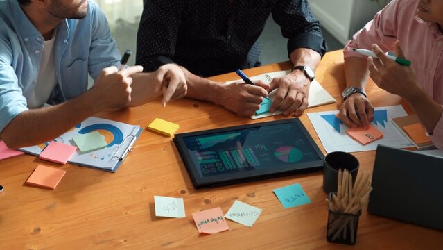 Closeup of business team hand brainstorm idea by using sticky notes at meeting table with tablet display financial graph. Group of diverse people planning about start up project strategy. Convocation.