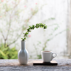 Coffee mug and leaves twig in a tall vase with backyard view