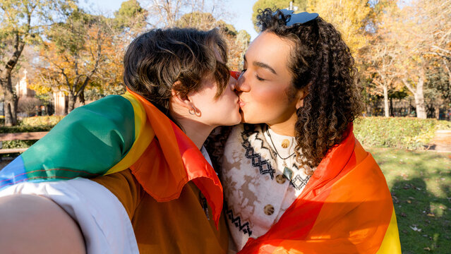 Lesbian couple sharing a kiss wrapped in rainbow flag