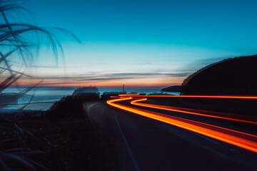 Slow shutter photo of car lights on a coast road © Adam