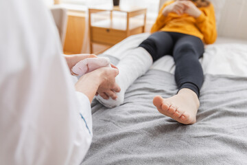 Girl with broken leg and doctor in clinic. Traumatologist orthopedist examines child leg in medical...