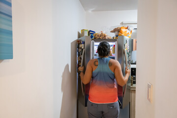 Woman looks at refrigerator full of fattening food. Concept of purpose, willpower