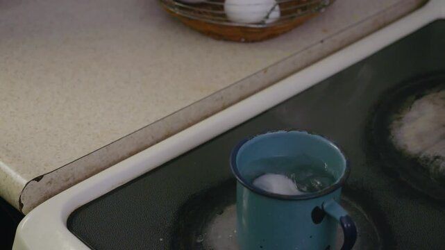 Metal cup with water, cooking an egg, on an electric stove.