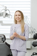 Dentist woman holding dental tools smiling in dental clinic