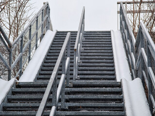 Snow-covered wide steel outdoor staircase with bicycle ramps on both sides, viewed from below under overcast winter sky. 