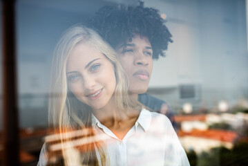 Couple gazing through window at home