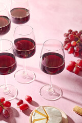 Red wine glasses, bunch of grapes and camembert cheese on pink background