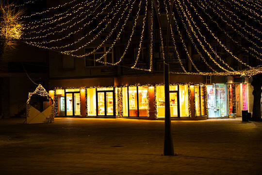 Festive City Square with Christmas String Lights and Illuminated Shops at Night in Korca, Albania 