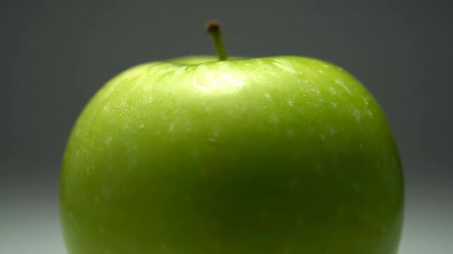 Close up of a green apple with stem against neutral background