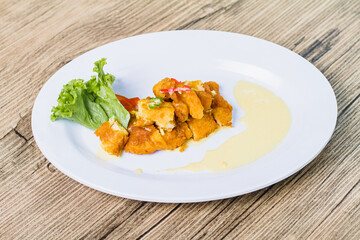 displays a serving of crispy chicken Karage on a white plate with a side of lettuce, tomato, and a creamy yellow sauce