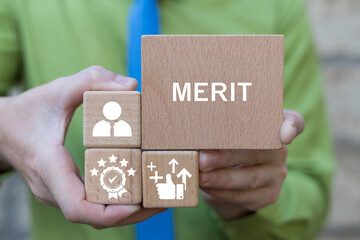 Business person holding wooden blocks sees the text MERIT. Merit Business and achievement concept. Demerit and merit evaluation, advantage and disadvantage in comparison.