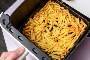 Hand pulls air fryer basket with golden french fries, crisp low oil side dish for quick family...
