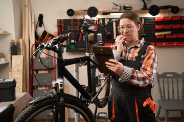 female mechanic repairing a bicycle using digital tablet gets nervous while reading information online and having trouble repairing a broken bike.
