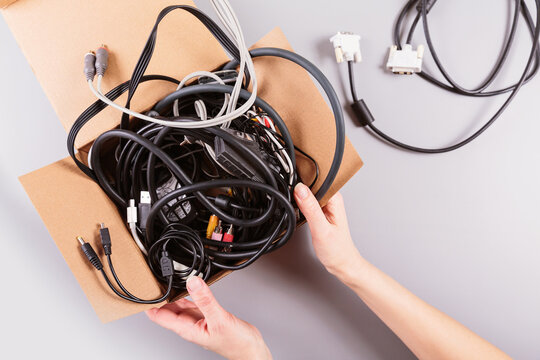 Woman's hands packing outdated gadgets and cables into a recycling container, demonstrating sustainable living choices