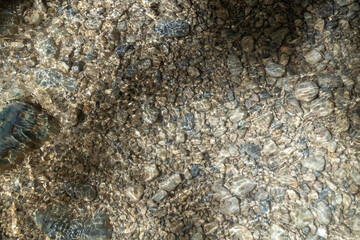 Top view of clear mountain water ripples over pebble stone bottom in Gizlikent Canyon. Natural sunlight patterns on river bed. September, Turkey.