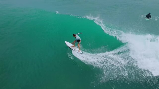Aerial Surfer Riding Emerald Wave, Carving Powerful Turn Along Reef Break With Cascading Whitewater And Spray,