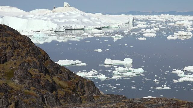 GREENLAND - 11.4.2025 - Great aerial timelapse of ice floes moving past a rock formation on Greenland's Disko Bay.