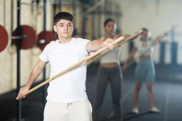 Young guy in sportswear doing warm-up with stick in gym