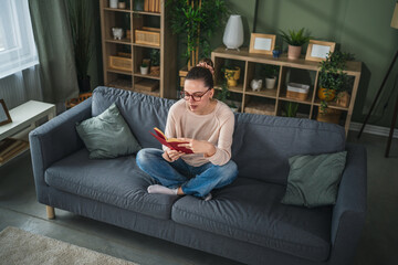 Obraz premium Young woman enjoying reading book on cozy sofa at home